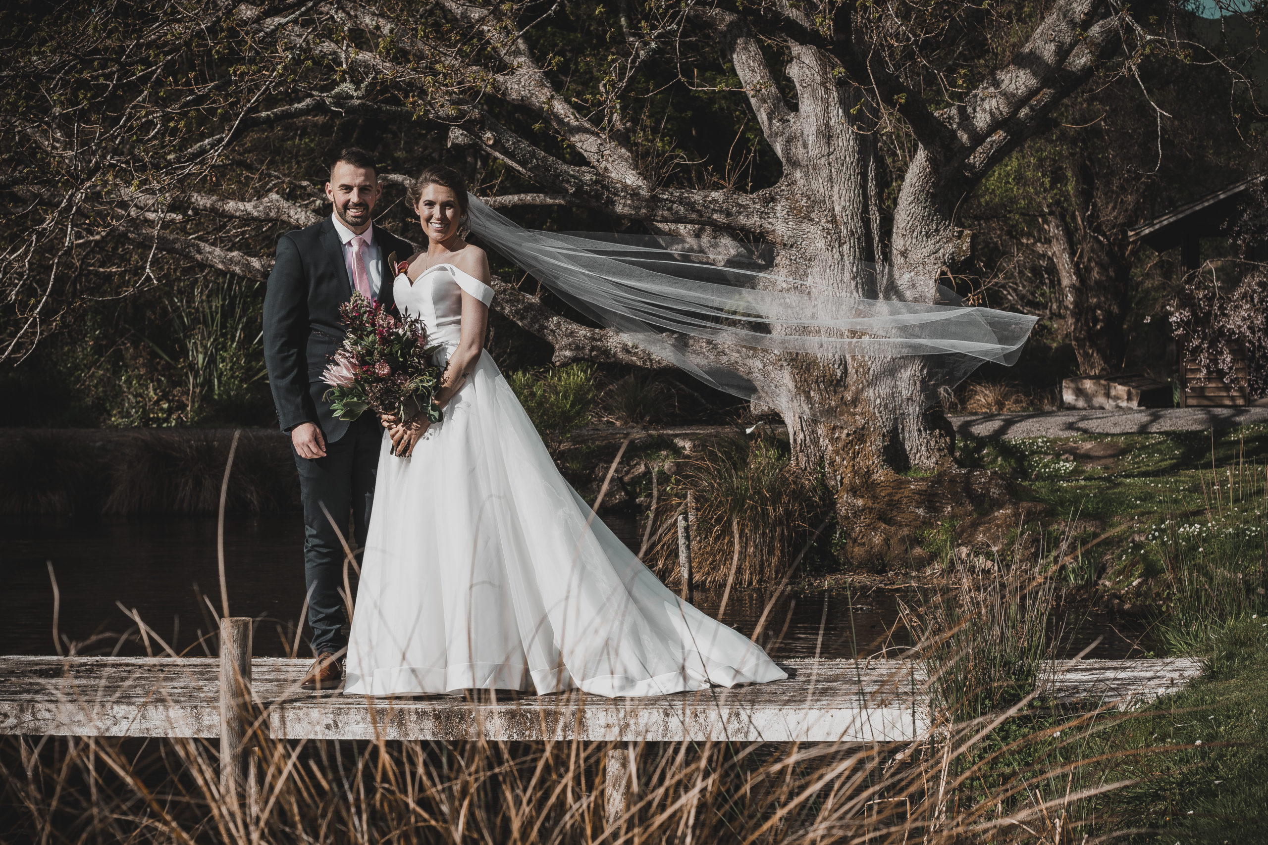 Bride and Groom on wooden wharf with veil blowing in the wind