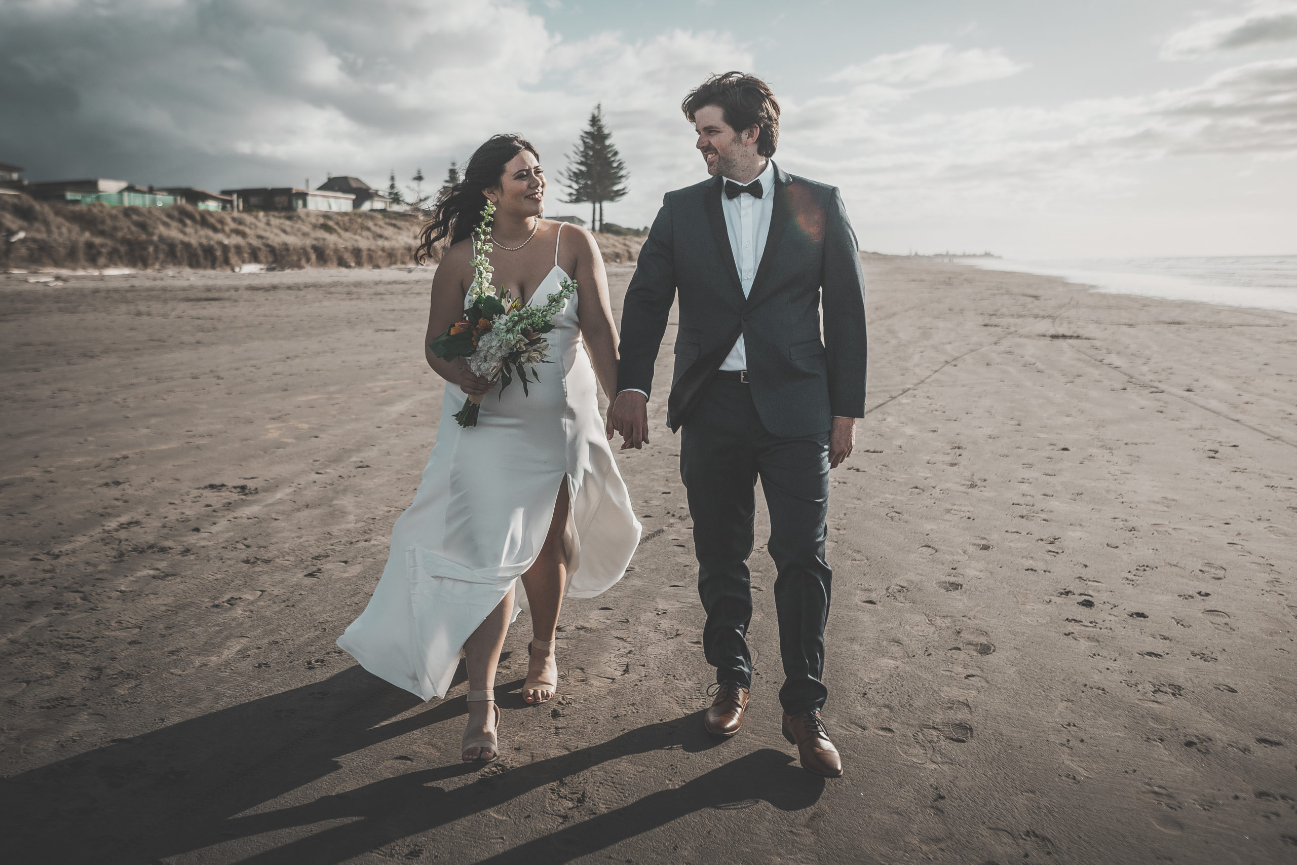Wedding couple walking down a beach looking happily at one another